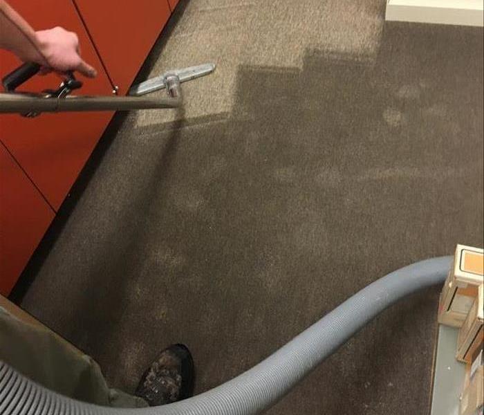 A technician using an extraction hose to remove water from a saturated carpet. 