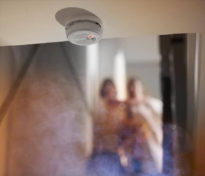 close-up of a smoke detector, with a family and smoke in the background